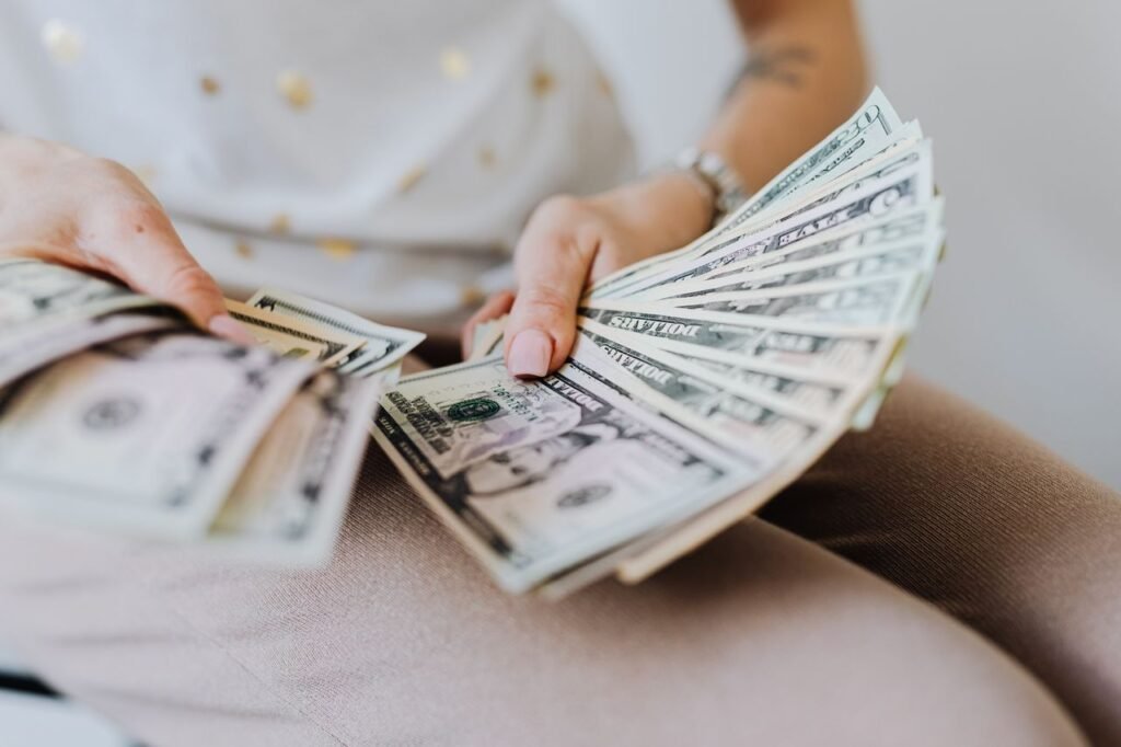 pexels-photo-4968668-4968668 Close-up of hands holding and counting US dollar bills indoors.