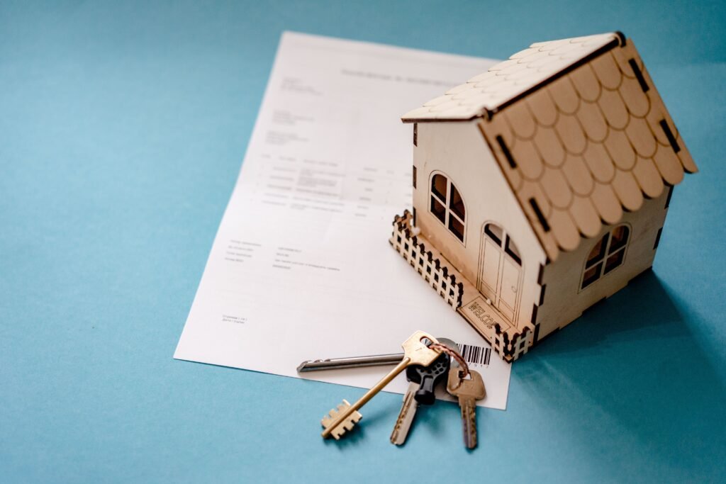 pexels-photo-12955837-12955837-1 Miniature wooden house with keys and contract symbolizing real estate transactions.
