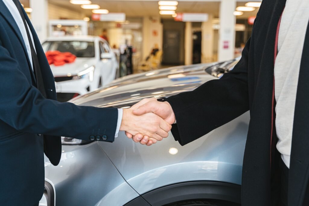 pexels-photo-7144199-7144199 Two businessmen shaking hands in a car dealership, sealing a deal.